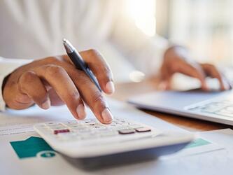 person using calculator and laptop while holding pen